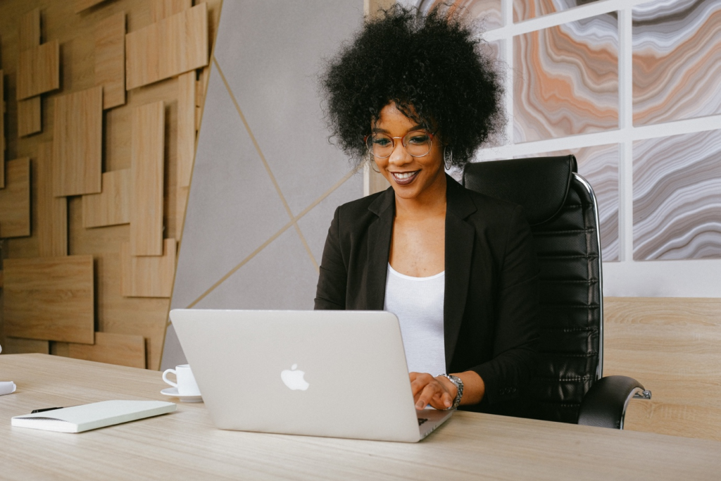 A woman in a black blazer smiling and using her MacBook